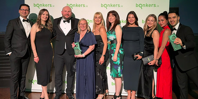 Ten people in formal attire pose in front of a bonkers.ie backdrop, with two people holding green awards.