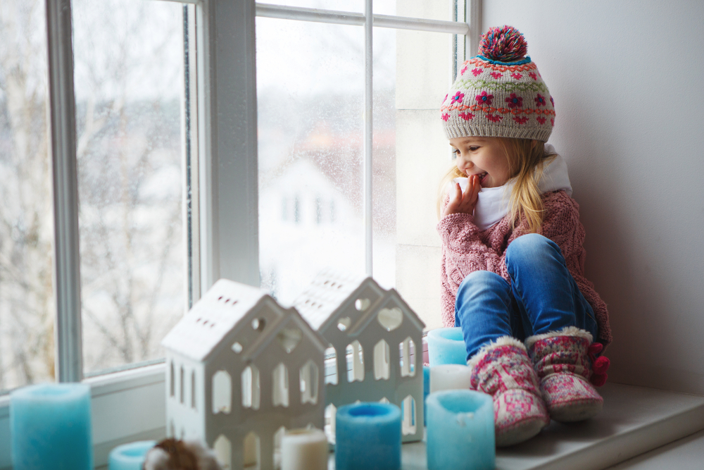 child sitting in window with winter clothes