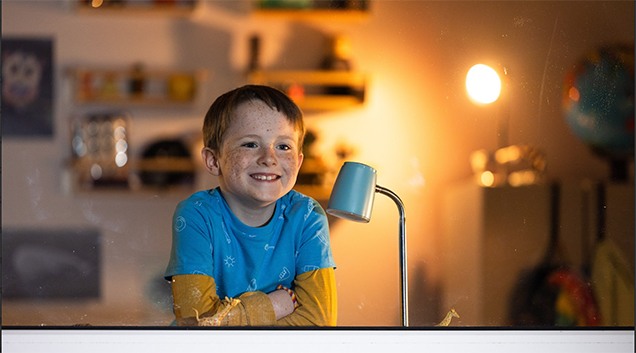 Young child smiling in bedroom with lamp