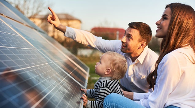 Family pointing at sun beside solar panel