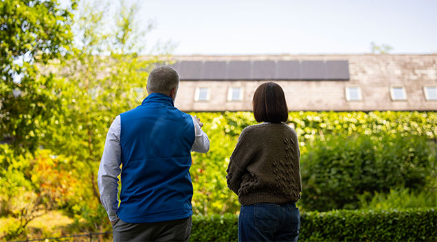 Two people looking at a house with solar panels on its roof